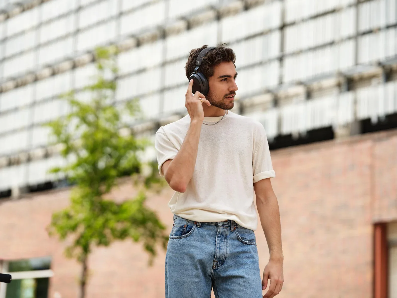 Man outdoors wearing Black Sennheiser MOMENTUM 4 Wireless headphones and touching the right ear cup